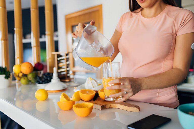 close up of a young pregnant woman pouring juice from a juicer into a drinking glass